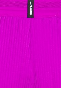 Shorts sportivi magenta con pieghe verticali, dotati di una vita nera con la scritta "NIKE RACING" e un logo. Tessuto morbido e leggero.