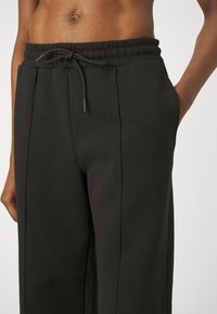 Svarta träningsoveraller gjorda av mjukt tyg, med en texturerad midjeband, justerbar dragsko och sidofickor samt rak benlängd.