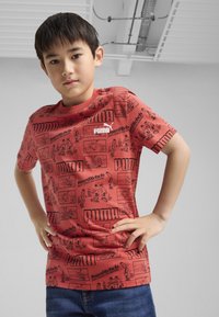 Raudona medvilninė marškinė su komiksų stiliaus grafika ir juodu spaudiniu, rodančiu logotipus "PUMA" ir "BoardRebels". Atsitiktinė siluetas su apykakle.