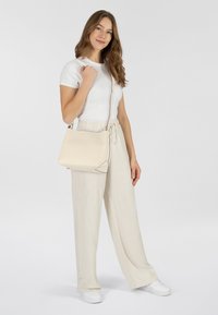 Borsa a tracolla in pelle beige con un design minimalista, caratterizzata da una forma pulita, cuciture sottili e una tracolla rimovibile.