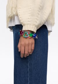 Pulsera de charms coloridos con formas de corazón y candado en materiales transparentes, unida a una cadena de plata, llevada en una mano.