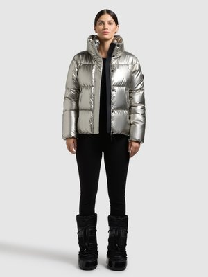 Silver, puffy, insulated jacket with a hood, zip front, and large quilted sections. Worn over black leggings and glossy black boots.