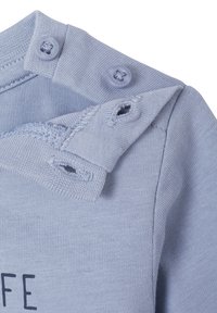 Himmelblaues Baumwollbekleidungsstück mit einer weichen Textur, das zwei Knopfverschlüsse an der Schulter und ein unvollendetes Saumdetail aufweist.