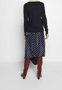 Granatowy sweter z długimi rękawami, zestawiony z granatową spódnicą o asymetrycznym kroju z białymi ukośnymi paskami oraz bordowymi kozakami na obcasie sięgającymi kolan.