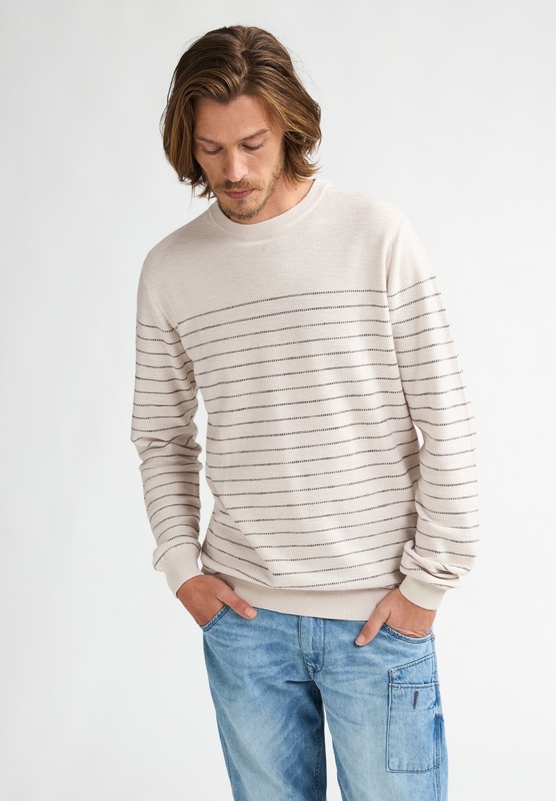 Felpa beige chiaro con strisce nere orizzontali, collo rotondo, maniche lunghe, polsini e orlo a costine, abbinata a jeans cargo azzurri.