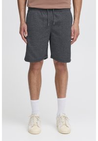 Pantaloncini in cotone grigio scuro con una texture liscia, vita elastica, tasche frontali e vestibilità comoda. Indossati con calzini bianchi alla caviglia e scarpe.