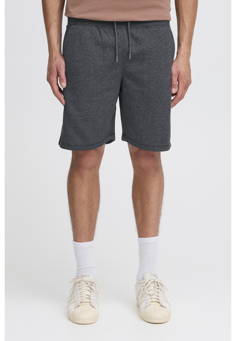 Pantaloncini in cotone grigio scuro con una texture liscia, vita elastica, tasche frontali e vestibilità comoda. Indossati con calzini bianchi alla caviglia e scarpe.