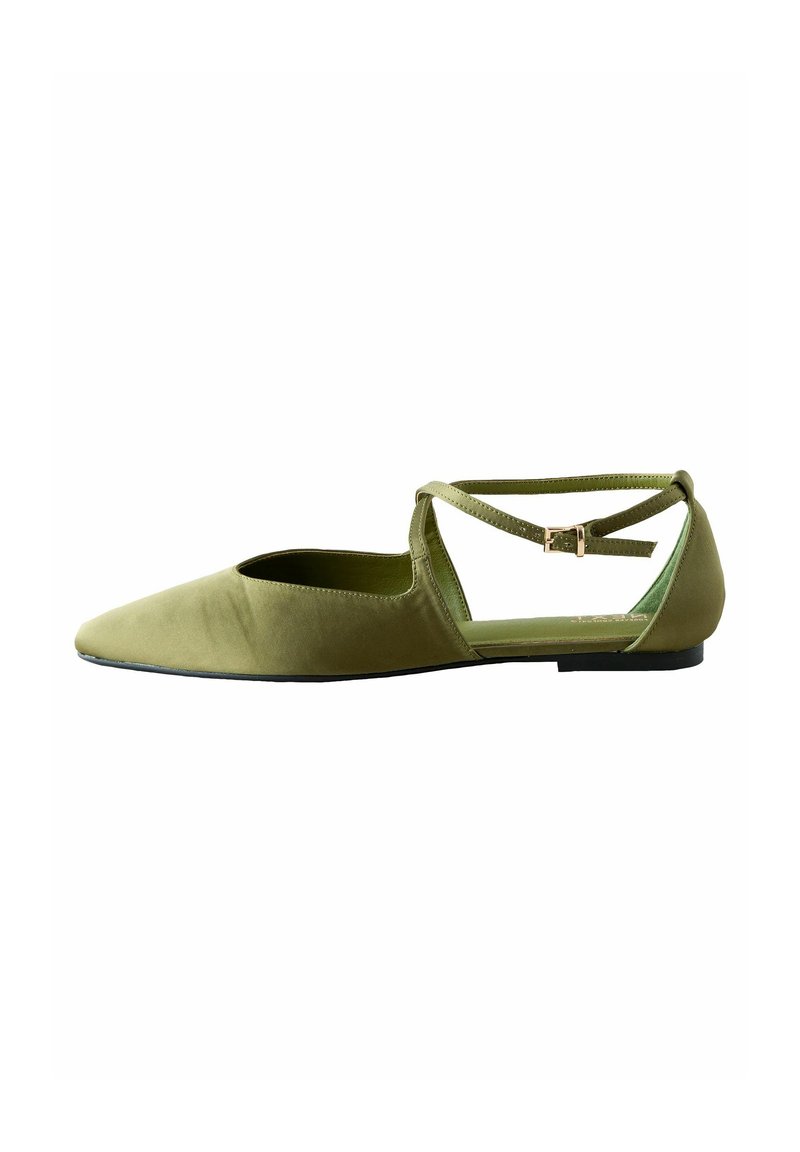 Zapato plano de tela color verde oliva, con punta afilada, diseño con lado abierto y tira cruzada en el tobillo, que incluye una pequeña hebilla.