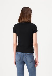 Un top negru cu mânecă scurtă, realizat dintr-un material fin, are un design ajustat și un guler rotund, fiind asociat cu blugi skinny albaștri.