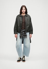 Czarna skórzana kurtka bombka, jasnoniebieskie zniszczone jeansy o szerokich nogawkach, brązowa koszula z guzikami, czarna i biała flanela związana w pasie, czarne sneakersy.