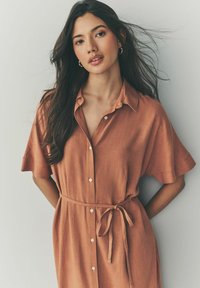 Robe à manches courtes et col boutonné en tissu orange rouille, dotée d'une ceinture à nouer à la taille et d'une texture subtile avec de petits boutons sur le devant.