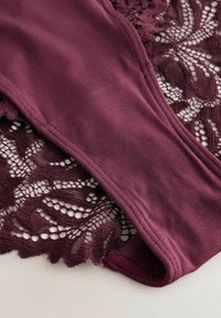 Dark purple cotton fabric with stitched seam overlaid on matching floral lace textile on a light background.