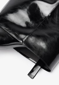 Must must nahk käekott, millel on sile, läikiv viimistlus, struktureeritud kuju ja kontrastne sisemine osa kitsaste käepidemetega.