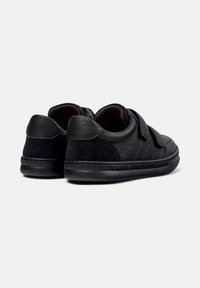 Chaussures noires en cuir et en daim avec une forme arrondie, dotées d'une sangle Velcro et d'accents texturés sur les côtés.