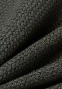 Dunkelgrüner, strukturierter Stoff mit einem gewebten Muster, das eine weiche, flauschige Oberfläche und sanfte Falten zeigt. Ideal für Wärme und Komfort.