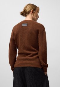 Brązowy sweter dzianinowy o miękkiej, puszystej teksturze i okrągłym dekolcie. Posiada małą, czarną metkę marki z tyłu.