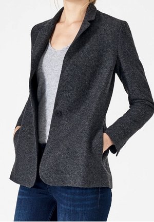 Grau gestreifter Blazer mit einer einzigen Knopfverschluss, angedeuteten Revers und zwei Seitentaschen. Über einem grauen Oberteil getragen und mit blauen Jeans kombiniert.