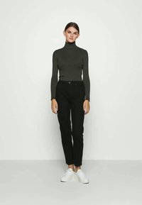 Juodos prigludusios džinsai, derinami su tamsiai pilku raukšlėtu golfo marškinėliu ir baltais sportiniais bateliais. Medžiaga lygi, su lieknu siluetu ir be raštų.