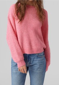 Rosa gestrickter Pullover mit geripptem Struktur, rundem Halsausschnitt und überschnittenen Schultern. Kombiniert mit Jeans in mittlerer Waschung.