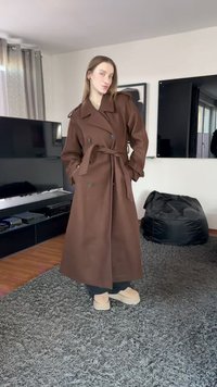 Brązowy dwurzędowy trencz z paskiem do wiązania, dużymi klapami i naramiennikami. W połączeniu z jasnymi butami na platformie.