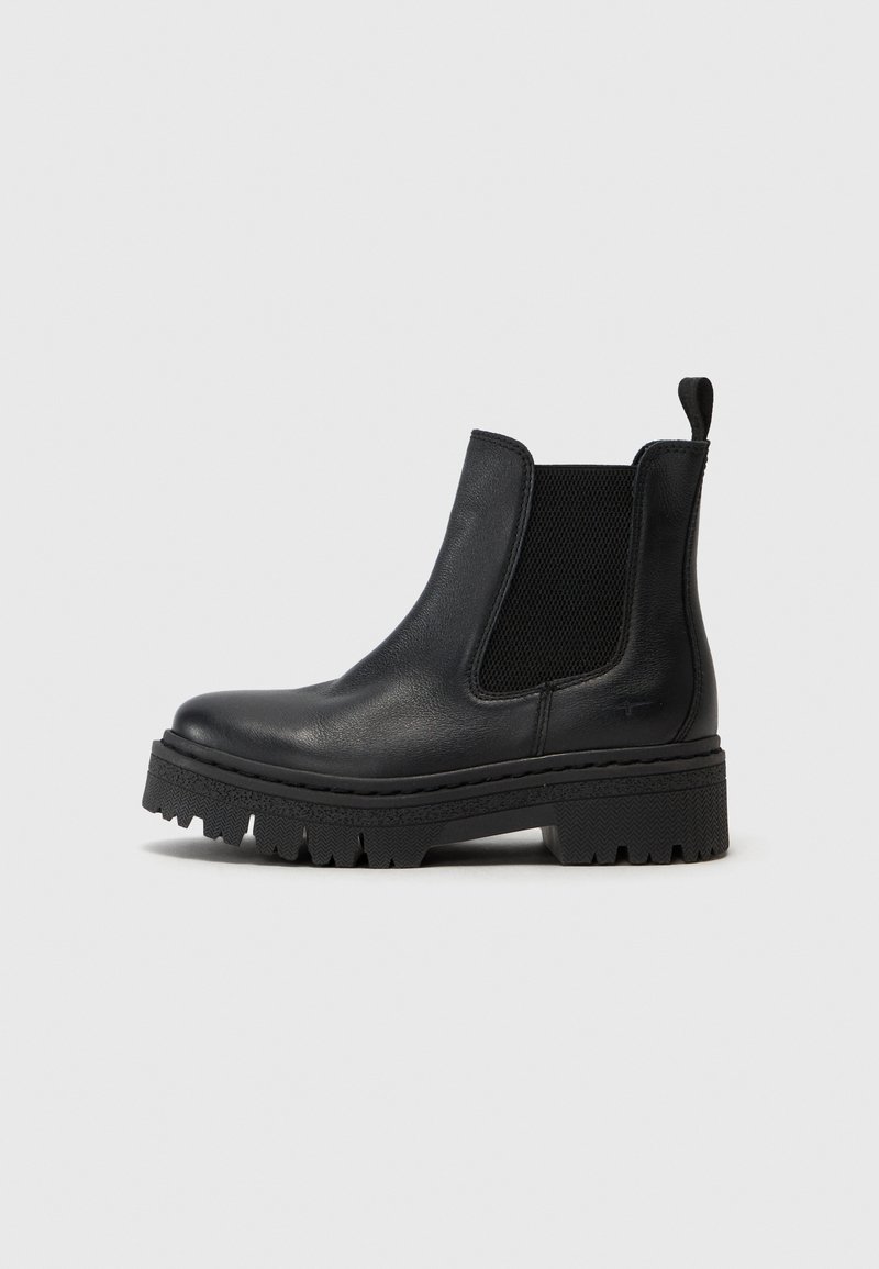 Bota de tornozelo em couro preto com painéis laterais elásticos, sola grossa e texturizada, e uma alça na parte de trás. Acabamento suave com um design robusto.