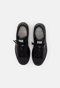 Zapatillas negras con un acabado de cuero suave, cordones planos y plantillas texturizadas con un patrón geométrico. Logotipo de Puma exhibido de manera prominente.