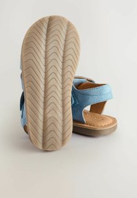 Blå mockask sandal med kardborreband, en beige läderinnersula och en strukturerad gummisål med zigzag-mönster.