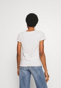 Gaiši pelēka T-kreklā, īsas piedurknes, apļveida kakla izgriezums, mīksta kokvilnas auduma, nedaudz saplaisājusi kakla izgriezuma un piedurkņu mala, kombinēta ar ziliem plaša griezuma džinsiem.