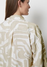 Light beige linen shirt with large white geometric patterns, featuring a back pleat, pointed collar, and dropped shoulders.