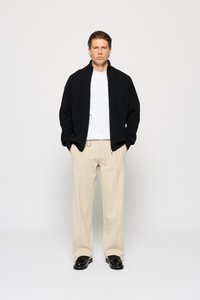 Sort, tekstureret cardigan med høj krave, båret over en hvid t-shirt. Sammen med beige bukser og sorte sko.