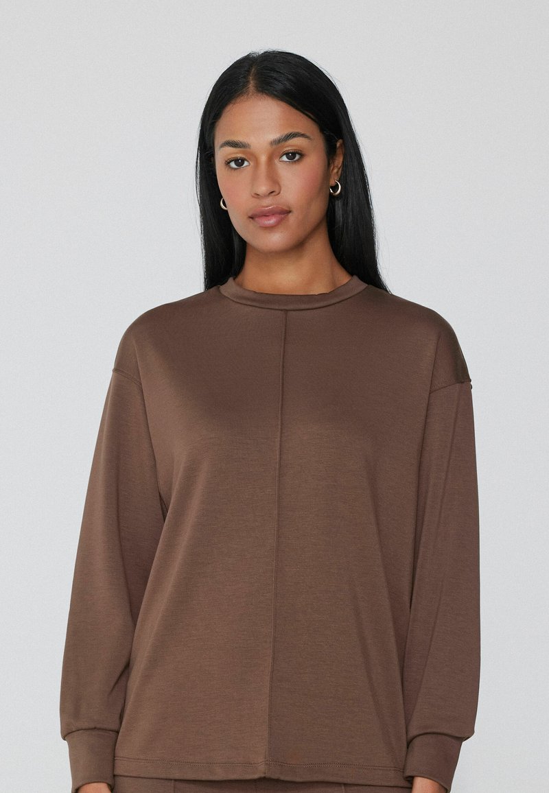 Maglietta marrone a maniche lunghe con scollo alto, texture morbida e vestibilità rilassata. Presenta dettagli di cuciture sottili e polsini alle maniche.