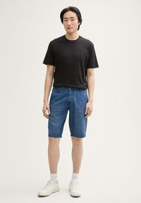 Zwarte korte mouwen T-shirt gecombineerd met blauwe denimshorts, met een relaxte pasvorm en opgerolde zomen, compleet met witte sneakers.