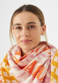 Écharpe colorée à motifs présentant des designs géométriques en rose, orange et jaune, fabriquée en tissu doux avec une finition texturée.