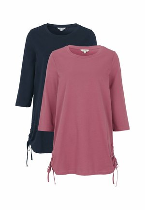 To tunikabluser med lange ærmer og snøre i siderne, den ene i afdæmpet pink og den anden i mørk marineblå, vist på hvid baggrund.