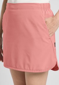 Gonna leggera rosa in tessuto, con vita elasticizzata, tasca laterale e orlo leggermente curvato per facilitare il movimento.