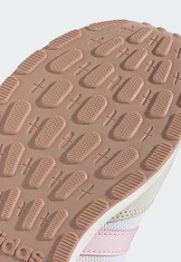 Đon Adidas tenisice s ružičastom gumom na bazi, s ovalnim uzorcima gaznoga sloja za prianjanje. Glatke teksture i svijetlosivi naglasci.