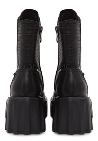 Stivali alla caviglia in pelle nera con design a coste, tacco a blocco alto e chiusura con zip sui lati. Finitura liscia e forma strutturata.