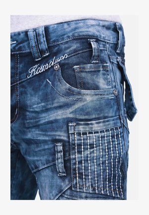 Dunkelblaue Jeans mit verblassten Akzenten, die mehrere Taschen, aufwendige Nähte an einer Tasche und ein sichtbares Markenlogo aufweisen.
