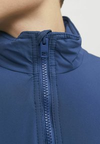 Marinblå jacka med hög krage, utrustad med en hel dragkedja och en smidig, mjuk tyggtextur. Enkelt, funktionellt designdetalj.