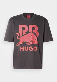 Dark gray cotton t-shirt featuring a large red logo with a bull and text “RR” and “HUGO” printed prominently. Short sleeves, crew neck design.