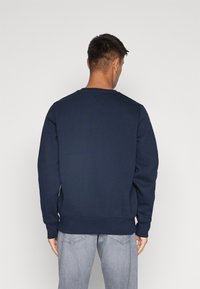 Granatowa bluza crewneck z długimi rękawami. Materiał z mieszanki bawełny, ściągacze na rękawach i u dołu, minimalistyczny design, gładka bez wzorów.