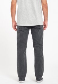 Los jeans gris oscuro tienen un diseño de pierna recta, cinco bolsillos y detalles de costura sutiles. Se llevan con una camiseta gris clara y zapatillas.