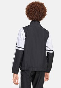 Zwart-witte windbreaker jas met een hoge kraag, elastische tailleband en gestreepte mouwen. Glad materiaal met een sportief ontwerp.