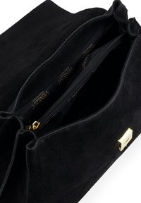 Sac à main en suède noir avec un compartiment zippé, présentant un accent en métal doré. Intérieur doublé de tissu affichant le logo de la marque.