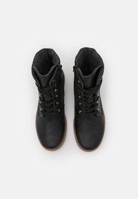 Bottes chelsea en cuir noir, avec un revêtement gris, présentant un design à lacets et des fermetures éclair sur les côtés. Semelles en caoutchouc avec une finition texturée.