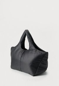 Sac à main noir matelassé avec poignées courtes, tissu doux et forme rectangulaire, photographié sur un fond uni clair.