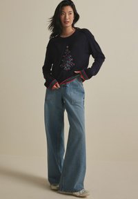 Marinblå tröja med en färgglad, broderad julgran-design, i kombination med vida ljusblå jeans. Flerfärgade randiga ärmslut och nederkant.