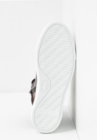 Chaussure en cuir marron avec une texture complexe, dotée d'une semelle en caoutchouc blanche avec un motif côtelé et un bout arrondi.