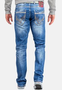 Blauwe denim jeans met lichte vervaging, voorzien van oranje stiksels en twee achterzakken met chevronpatronen. Draag ze met witte sneakers.