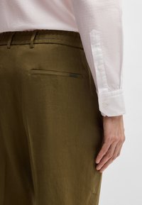 Light pink textured shirt with long sleeves, paired with olive green, smooth fabric trousers featuring a rear pocket and subtle branding detail.